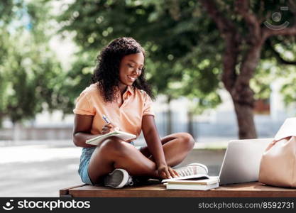 technology, education and people concept - happy smiling african american student girl with notebook, laptop computer and books in city. african student girl with laptop and books in city