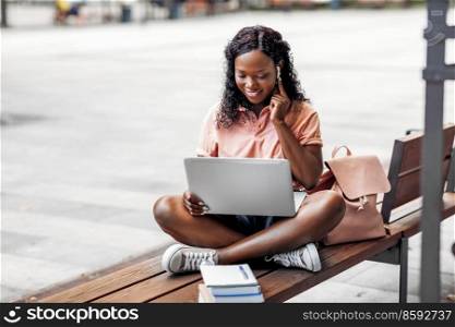 technology, education and people concept - happy smiling african american student girl in earphones with laptop computer and books in city. african student girl in earphones with laptop
