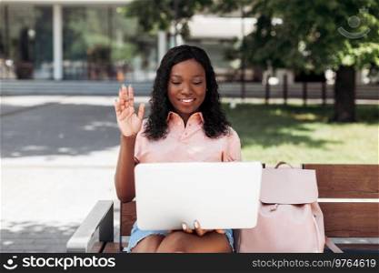 technology, education and people concept - happy smiling african american student girl with laptop compute having video call in city. african student girl with laptop having video call