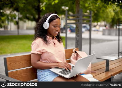 technology, education and people concept - happy smiling african american student girl in headphones with laptop computer and books in city. african student girl in headphones with laptop