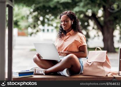 technology, education and people concept - happy smiling african american student girl in earphones with laptop computer and books in city. african student girl in earphones with laptop