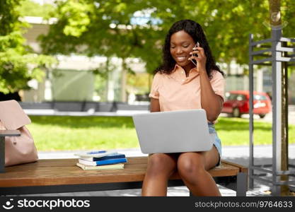 technology, education and people concept - happy smiling african american student girl with laptop computer and books calling on smartphone in city. african student girl calling on smartphone in city