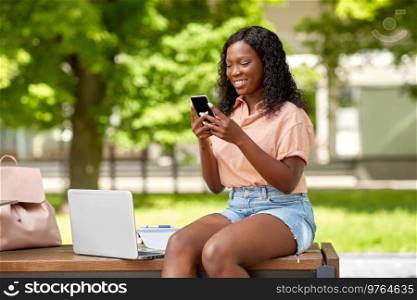 technology, education and people concept - happy smiling african american student girl with smartphone and laptop computer in city. african student girl with laptop and smartphone