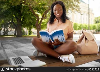 technology, education and people concept - happy smiling african american student girl reading book in city. african student girl reading book in city