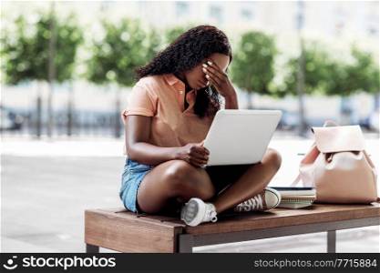 technology, education and people concept - sad african american student girl with laptop computer and books in city. african student girl with laptop and books in city