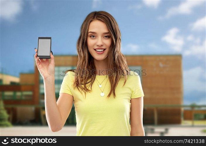 technology, education and people concept - smiling young woman or teenage girl in yellow t-shirt holding smartphone with blank screen over school background. teenage girl holding smartphone over school