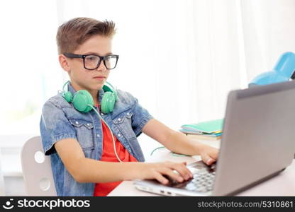 technology, education and people concept - student boy in glasses with headphones typing on laptop computer at home. student boy in glasses typing on laptop at home