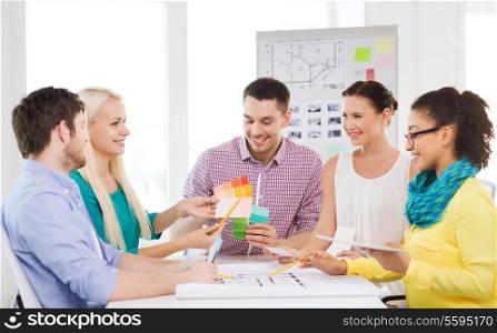 technology, education, interior design and office concept - smiling interior designers with color samples, blueprint and tablet pc in office