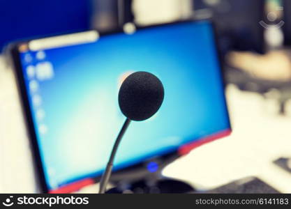 technology, electronics and audio equipment concept - close up of microphone and computer monitor at recording studio or radio station