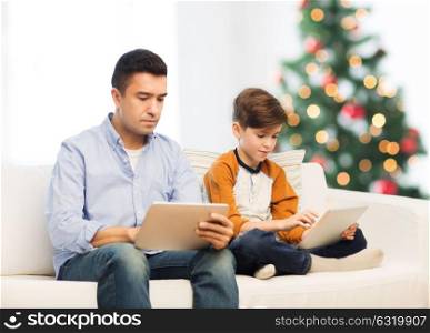 technology, family and people concept - father and son with tablet pc computer networking or playing at home over christmas tree background. father and son with tablet pc at christmas
