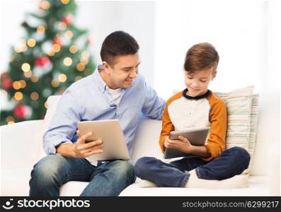 technology, family and people concept - happy father and son with tablet pc computer networking or playing at home over christmas tree background. happy father and son with tablet pc at christmas