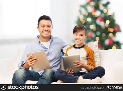technology, family and people concept - happy father and son with tablet pc computer networking or playing at home over christmas tree background. happy father and son with tablet pc at christmas