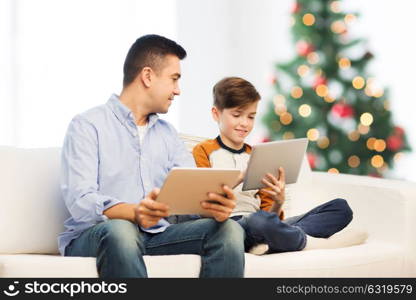 technology, family and people concept - happy father and son with tablet pc computer networking or playing at home over christmas tree background. happy father and son with tablet pc at christmas