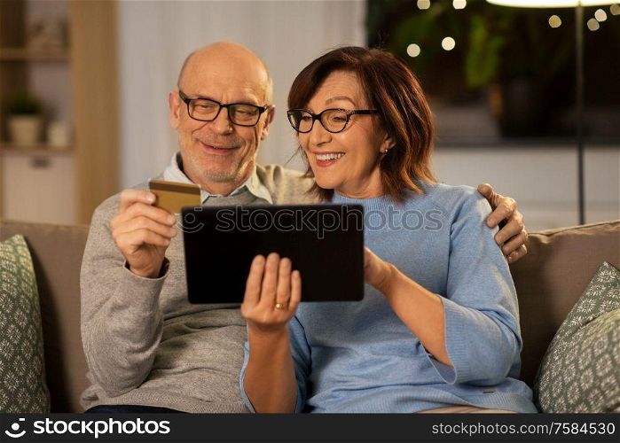 technology, finance and people concept - happy smiling senior couple with tablet pc computer and credit card at home in evening. happy senior couple with tablet pc and credit card