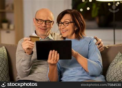 technology, finance and people concept - happy smiling senior couple with tablet pc computer and credit card at home in evening. happy senior couple with tablet pc and credit card