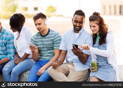 technology, friendship and international concept - group of friends with smartphones hanging out in summer city. friends with smartphones hanging out in summer