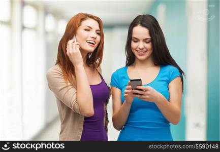technology, friendship and leisure concept - two smiling teenagers with smartphones texting and calling
