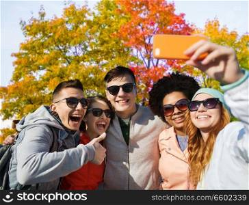 technology, friendship and people concept - happy friends taking selfie by smartphone over autumn park background. friends taking selfie by smartphone in autumn park