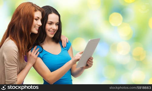 technology, friendship and people concept - two smiling teenage girls or young women pointing finger at tablet pc computer screen over green lights background