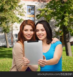 technology, friendship and people concept - two smiling teenagers taking picture with tablet pc camera
