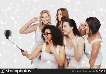 technology, friendship, body positive and people concept - group of happy women in white underwear taking picture with smartphoone on selfie stick over snow