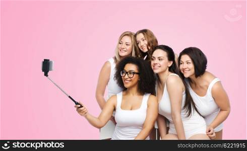 technology, friendship, body positive and people concept - group of happy women in white underwear taking picture with smartphoone on selfie stick over pink background