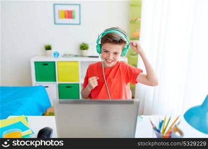 technology, gaming and people concept - boy in headphones playing video game on laptop computer and celebrating victory at home. boy in headphones playing video game on laptop