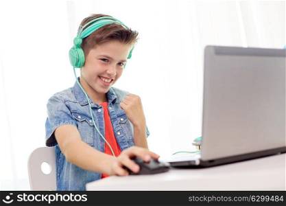 technology, gaming and people concept - boy in headphones playing video game on laptop computer and celebrating victory at home. boy in headphones playing video game on laptop