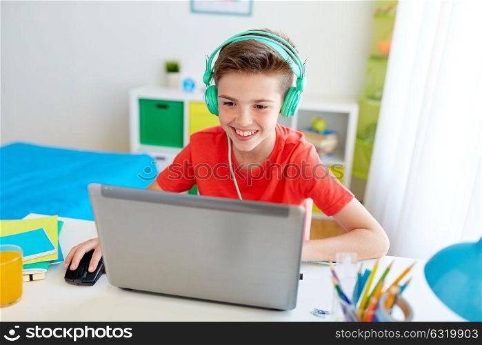 technology, gaming and people concept - boy in headphones playing video game on laptop computer at home. boy in headphones playing video game on laptop