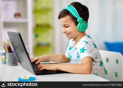 technology, gaming and people concept - boy in headphones playing video game on laptop computer at home. boy in headphones playing video game on laptop