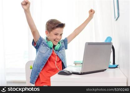 technology, gaming and people concept - boy with headphones playing video game on laptop computer and celebrating victory at home. boy with headphones playing video game on laptop