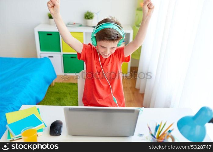 technology, gaming and people concept - boy with headphones playing video game on laptop computer and celebrating victory at home. boy with headphones playing video game on laptop