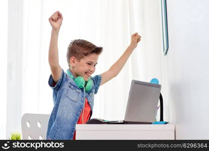 technology, gaming and people concept - boy with headphones playing video game on laptop computer and celebrating victory at home. boy with headphones playing video game on laptop