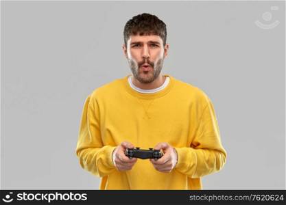 technology, gaming and people concept - young man or gamer with gamepad playing video game over grey background. man or gamer with gamepad playing video game