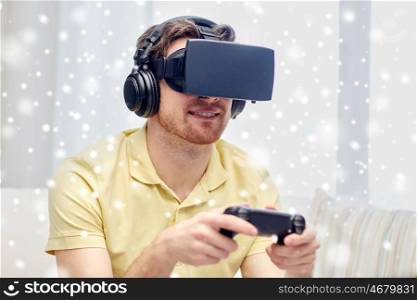 technology, gaming, augmented reality, entertainment and people concept - happy young man in headphones with virtual headset or 3d glasses playing video game with controller gamepad at home over snow