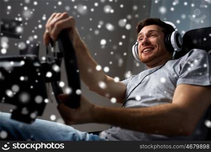 technology, gaming, entertainment and people concept - happy smiling young man in headphones with pc computer playing car racing video game at home and steering wheel over snow