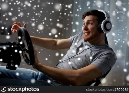 technology, gaming, entertainment and people concept - happy smiling young man in headphones with pc computer playing car racing video game at home and steering wheel over snow