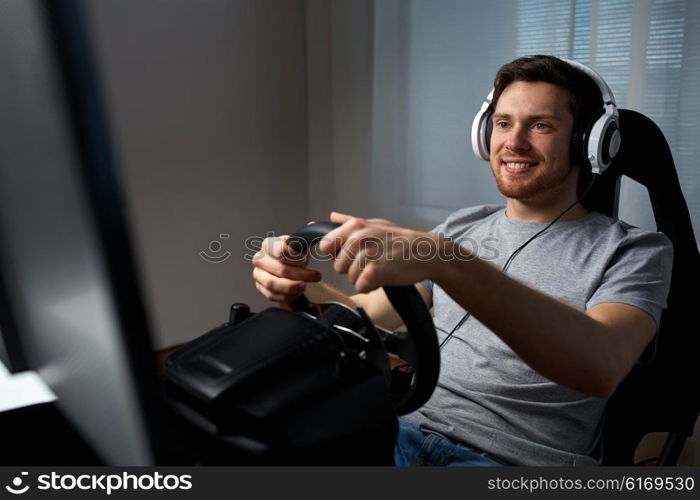 technology, gaming, entertainment and people concept - happy smiling young man in headphones with pc computer playing car racing video game at home and steering wheel