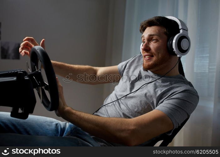 technology, gaming, entertainment and people concept - happy smiling young man in headphones with pc computer playing car racing video game at home and steering wheel