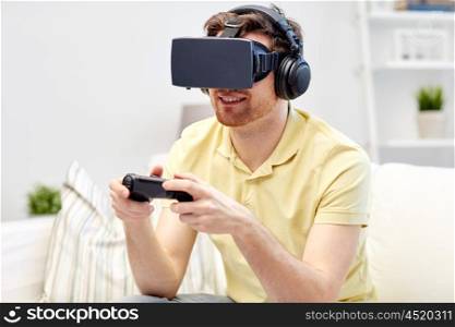 technology, gaming, entertainment and people concept - happy young man with virtual reality headset or 3d glasses playing video game with controller gamepad at home