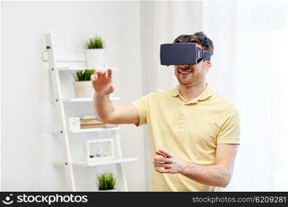 technology, gaming, entertainment and people concept - happy young man with virtual reality headset or 3d glasses playing video game at home