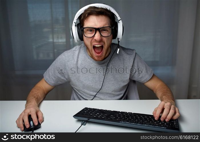 technology, gaming, entertainment, let&amp;#39;s play and people concept - angry screaming young man in headset with pc computer playing game at home and streaming playthrough or walkthrough video