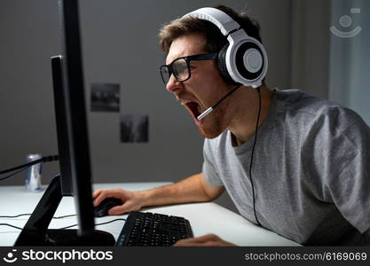 technology, gaming, entertainment, let&amp;#39;s play and people concept - angry screaming young man in headset with pc computer playing game at home and streaming playthrough or walkthrough video