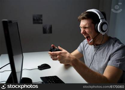 technology, gaming, entertainment, let&amp;#39;s play and people concept - angry screaming young man in headset with controller gamepad playing computer game at home and streaming playthrough video