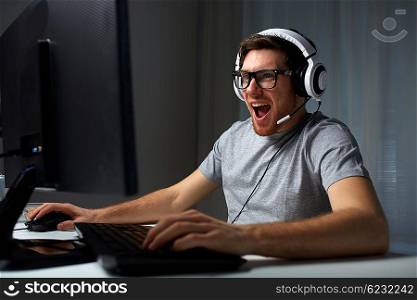 technology, gaming, entertainment, let&amp;#39;s play and people concept - happy laughing young man in eyeglasses with headset playing computer game at home and streaming playthrough or walkthrough video