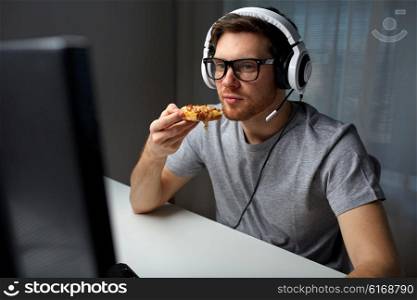 technology, gaming, entertainment, let&amp;#39;s play and people concept - young man in headset with pc computer eating pizza while playing game at home and streaming playthrough or walkthrough video