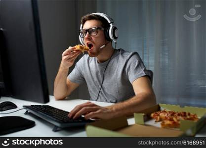technology, gaming, entertainment, let&amp;#39;s play and people concept - young man in headset with pc computer eating pizza while playing game at home and streaming playthrough or walkthrough video