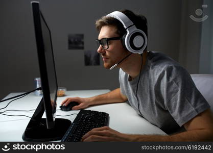 technology, gaming, entertainment, let&amp;#39;s play and people concept - young man in headset and glasses with pc computer playing game at home and streaming playthrough or walkthrough video