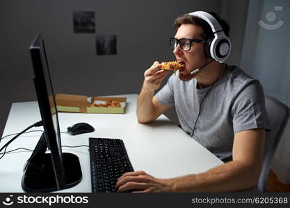 technology, gaming, entertainment, let&amp;#39;s play and people concept - young man in headset with pc computer eating pizza while playing game at home and streaming playthrough or walkthrough video