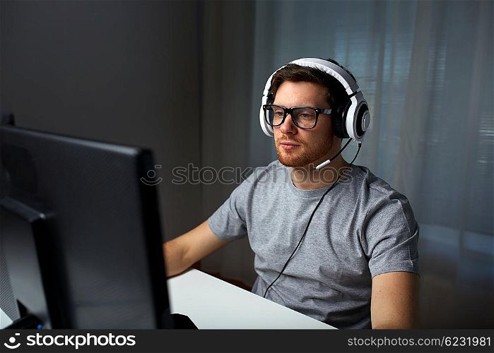 technology, gaming, entertainment, let&amp;#39;s play and people concept - young man in headset and glasses with pc computer playing game at home and streaming playthrough or walkthrough video